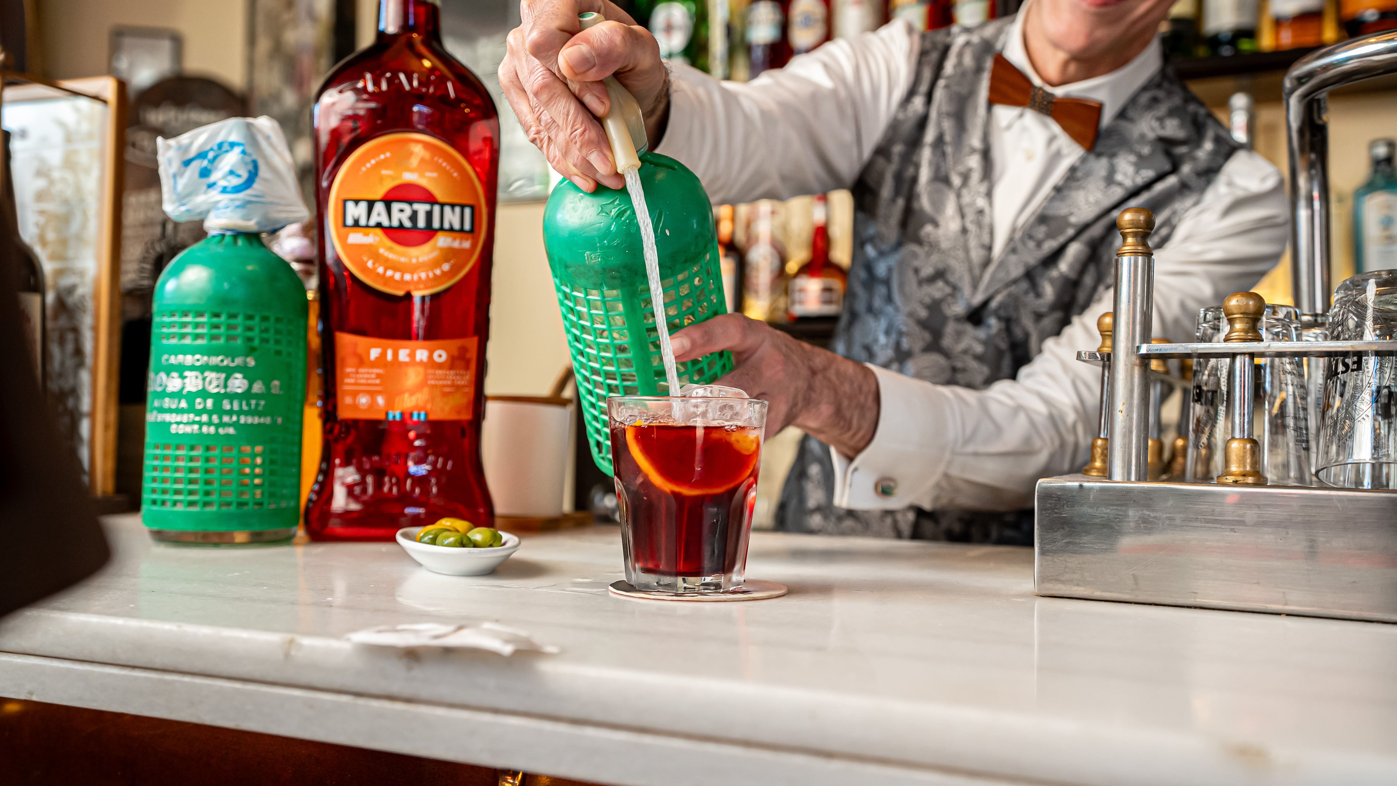 Bartender preparing red vermouth with ice and orange at a bar counter